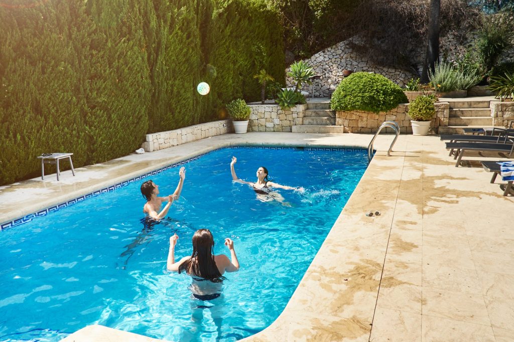 mature woman throwing ball with son and daughter in swimming pool